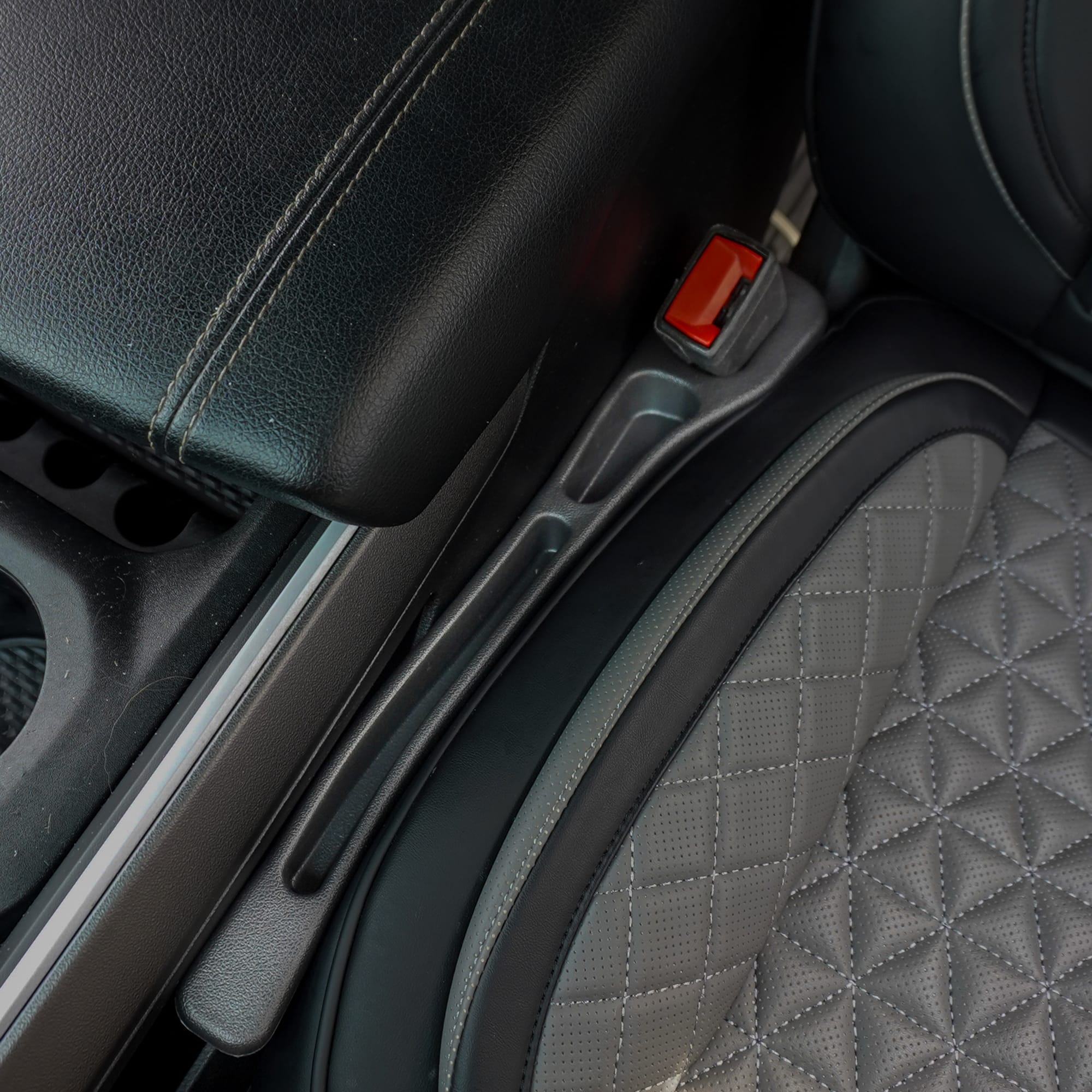Close-up of a car seat with a diamond pattern and a red seat belt buckle.